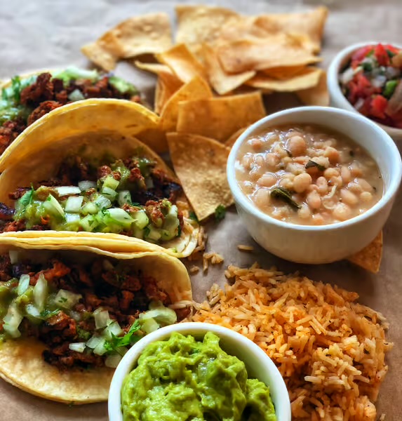The al pastor plate — chips, beans, guacamole, and the salsa rotation of the day.